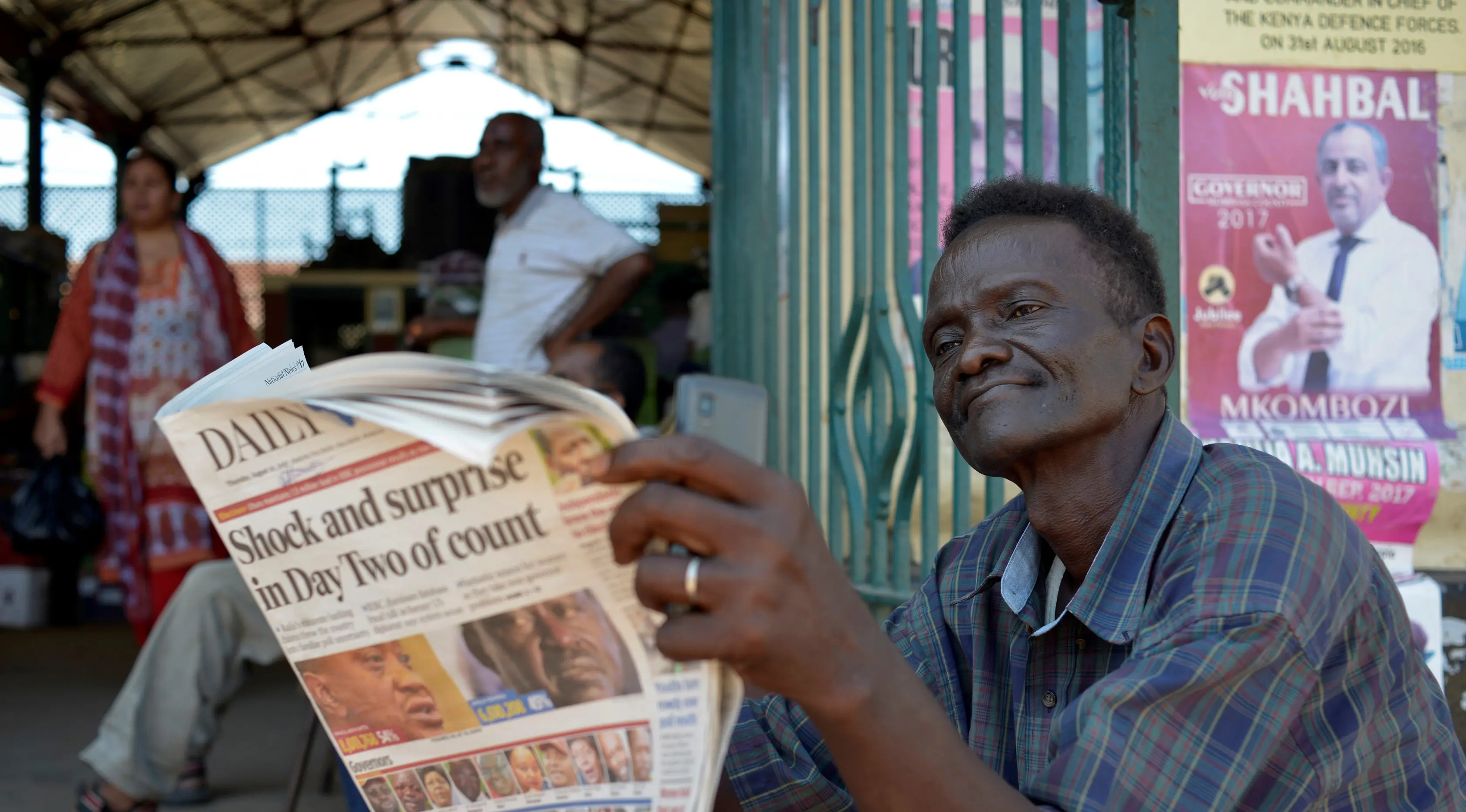 Seorang pria membaca koran sambil menunggu hasil resmi pemilihan umum Kenya di luar pasar sentral di Mombasa (10/8). Warga Kenya tengah menunggu hasil pemilihan presidennya, antara Uhuru Kenyatta dan pesaingnya, Raila Odinga. (AFP Photo/Tobin Jones)