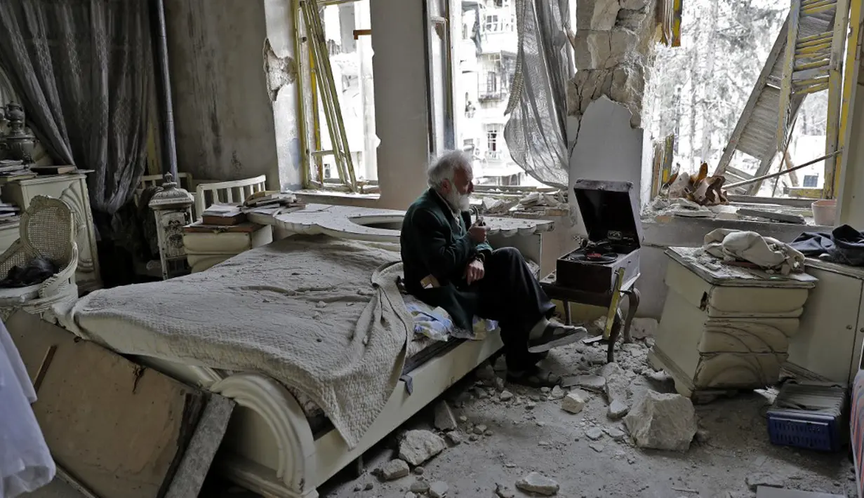 Mohammed Mohiedin Anis atau Abu Omar (70) merokok sambil mendengarkan musik saat duduk di kamar tidurnya yang hancur di lingkungan yang sebelumnya dikuasai pemberontak, al-Shaar, Aleppo, Suriah, 9 Maret 2017. (Photo by JOSEPH EID/AFP)
