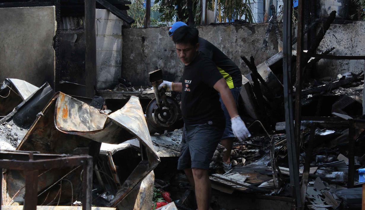Dua orang pria yang berprofesi sebagai penagih utang atau mata elang (matel) mencoba memberhentikan seorang pemilik kendaraan yang kreditnya bermasalah. Tampak dalam foto, pemilik kios membersihkan puing-puing bangunan usai kebakaran yang melanda deretan kios di kawasan Kalibata, Jakarta Selatan, pada Jumat (12/12/2025). (merdeka.com/magang/Rendi Saputra)