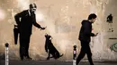 Seorang pria berjalan melewati mural yang diduga karya seniman sekaligus aktivis Banksy di Paris, Prancis, Minggu (24/6). Tujuh mural terbaru telah ditemukan di Paris dalam beberapa hari terakhir. (PHILIPPE LOPEZ/AFP)
