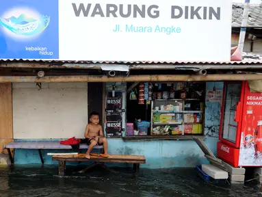 Seorang anak duduk di depan rumahnya yang tergenang air di Kawasan Muara Angke, Jakarta, Rabu (11/1). Banjir yang terjadi hampir setiap hari dalam satu bulan terakhir akibat rob yang diperparah dengan jebolnya tanggul. (Liputan6.com/Gempur M. Surya)