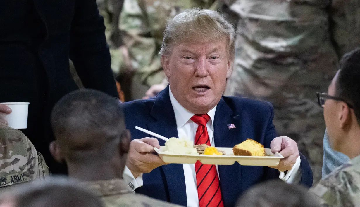 <p>Presiden Amerika Serikat Donald Trump mengangkat nampan makan malam saat mengunjungi Pangkalan Udara Bagram, Afghanistan, Kamis (28/11/2019). Kunjungan dadakan Trump pada hari Thanksgiving tersebut mengejutkan pasukan AS yang bertugas di Afghanistan. (AP Photo/Alex Brandon)</p>