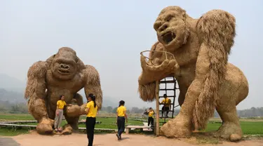 Para siswa berfoto dengan patung King Kong raksasa yang terbuat dari jerami di Huay Teung Tao Lake, Don Kaeo, Chiang Mai, Thailand, Rabu (3/4). Tempat ini merupakan satu dari banyak spot foto instagramable di Chiang Mai. (Lillian SUWANRUMPHA/AFP)