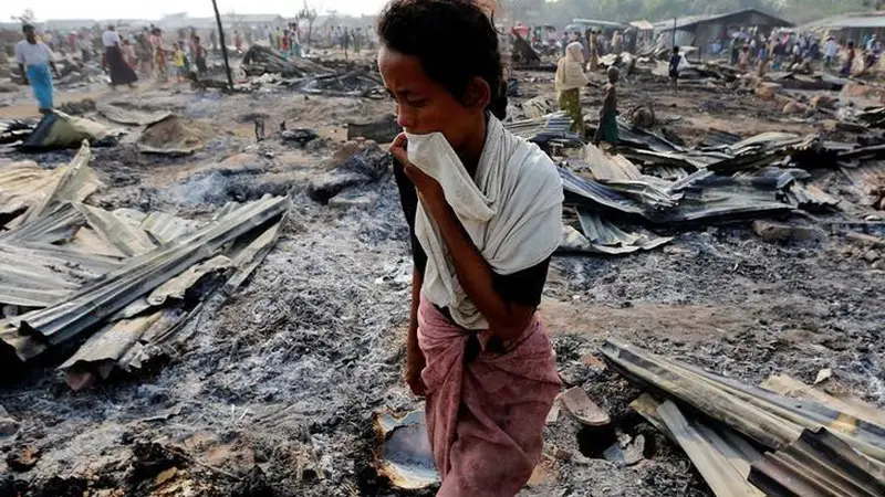 Seorang perempuan berjalan di antara puing-puing kebakaran kamp pengungsi Rohingya di Rakhine pada 3 Mei 2016 