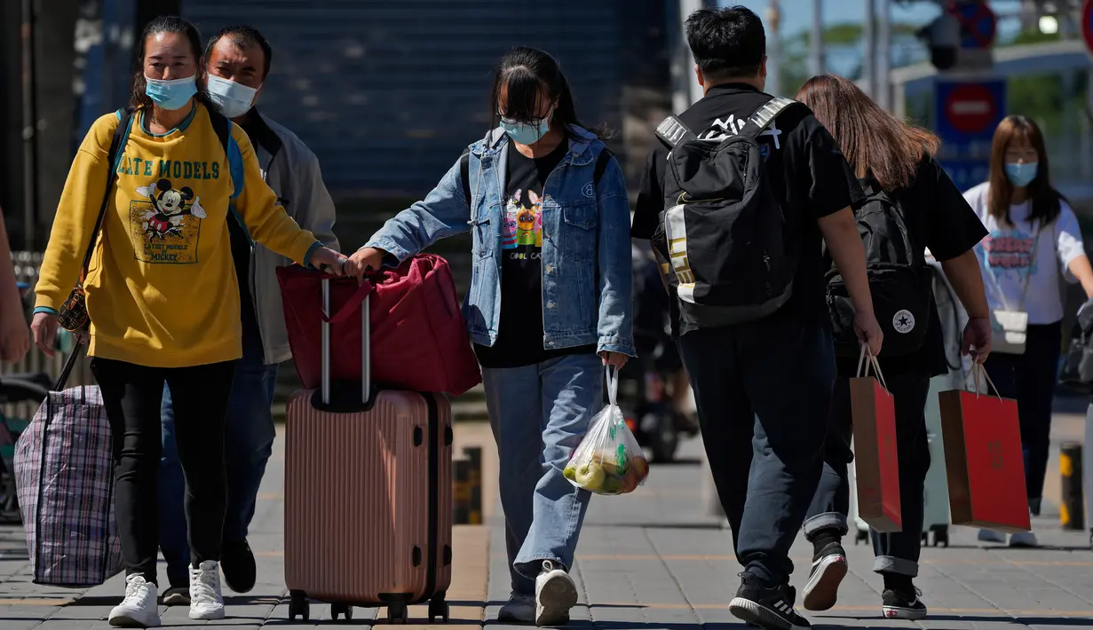 Wisatawan mengenakan masker wajah dengan barang bawaan mereka meninggalkan stasiun kereta api Beijing di Beijing, Selasa (6/9/2022). China lockdown jutaan warganya di bawah pembatasan ketat COVID-19. (AP Photo/Andy Wong)