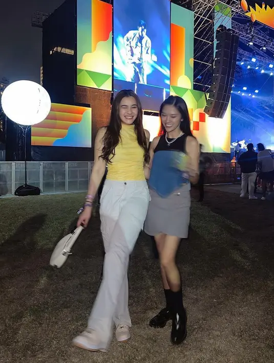Aaliyah Massaid hadir di festival musik dengan mengenakan atasan halter neck kuning dipadukan celana putih panjang serasi dengan sepatu dan mini bagnya. [@aaliya.massaid]