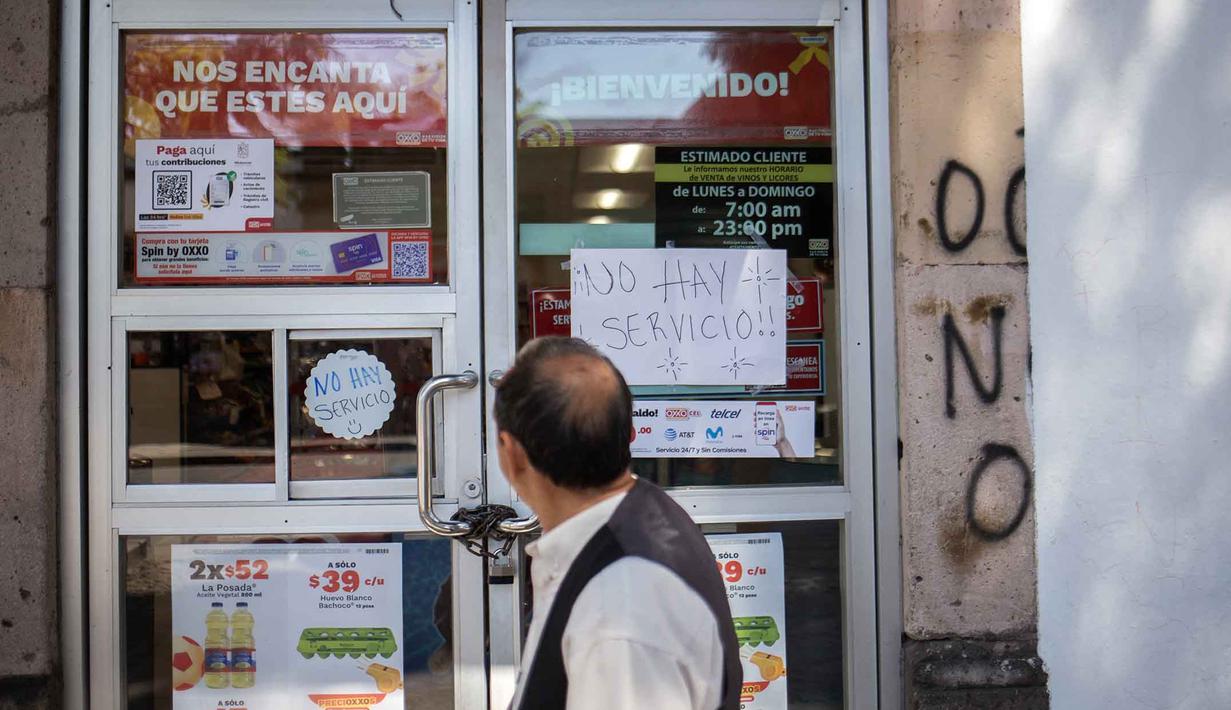 Kelompok bersenjata yang diduga pendukung Nemesio Ruben Oseguera Cervantes alias "El Mencho" memblokir jalan tol di beberapa negara bagian serta membakar kendaraan dan tempat usaha. Tampak dalam foto, seorang pria berjalan melewati toko yang tutup dengan tanda bertuliskan "Tidak ada layanan" di Morelia, negara bagian Michoacan, Meksiko, pada 23 Februari 2026. (Enrique Castro/AFP)