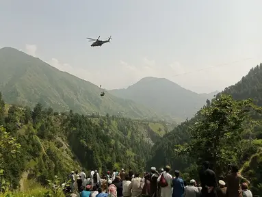 Orang-orang menyaksikan seorang tentara terjun dari helikopter selama misi penyelamatan untuk menyelamatkan para siswa yang terjebak di keeta gantung di desa Pashto di provinsi pegunungan Khyber Pakhtunkhwa, pada 22 Agustus 2023. (AFP)