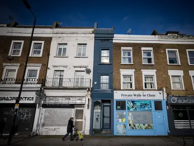 Seorang pejalan kaki melewati bagian depan bangunan yang dijuluki "Rumah Tersempit di London" (cat biru) di London barat pada 5 Februari 2021. Terjepit di antara praktek dokter dan salon penata rambut, rumah mungil tersebut hanya memiliki lebar 1,6 meter dan panjang 7,31 meter. (Tolga Akmen/AFP)