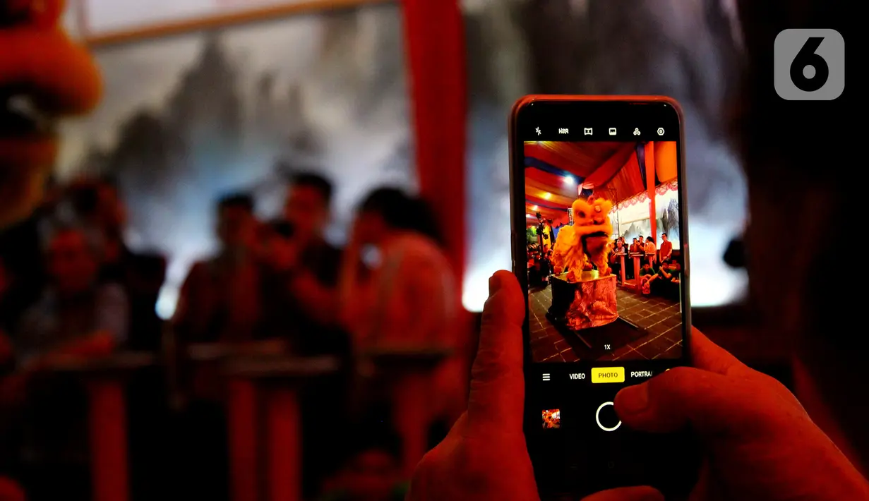 Pengunjung memotret atraksi barongsai yang tampil di Vihara Dhanagun pada malam Tahun Baru Imlek 2571 di Bogor, Jawa Barat, Jumat (24/1/2020). Atraksi dilakukan  Grup Atraksi Seni Indonesia (GASI) untuk menghibur jemaah yang bersembahyang selama malam Imlek. (merdeka.com/magang/Muhammad Fayyadh)