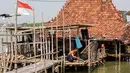 Situasi ini sudah terjadi sejak 2014, wilayah yang dulunya pemukiman dan sawah kini berubah total menjadi perairan. Tampak dalam foto, seorang pria bekerja di luar rumah yang sebagian terendam air laut akibat banjir pasang di desa Timbulsloko, Demak, Jawa Tengah pada Sabtu 18 April 2026. (DEVI RAHMAN/AFP)