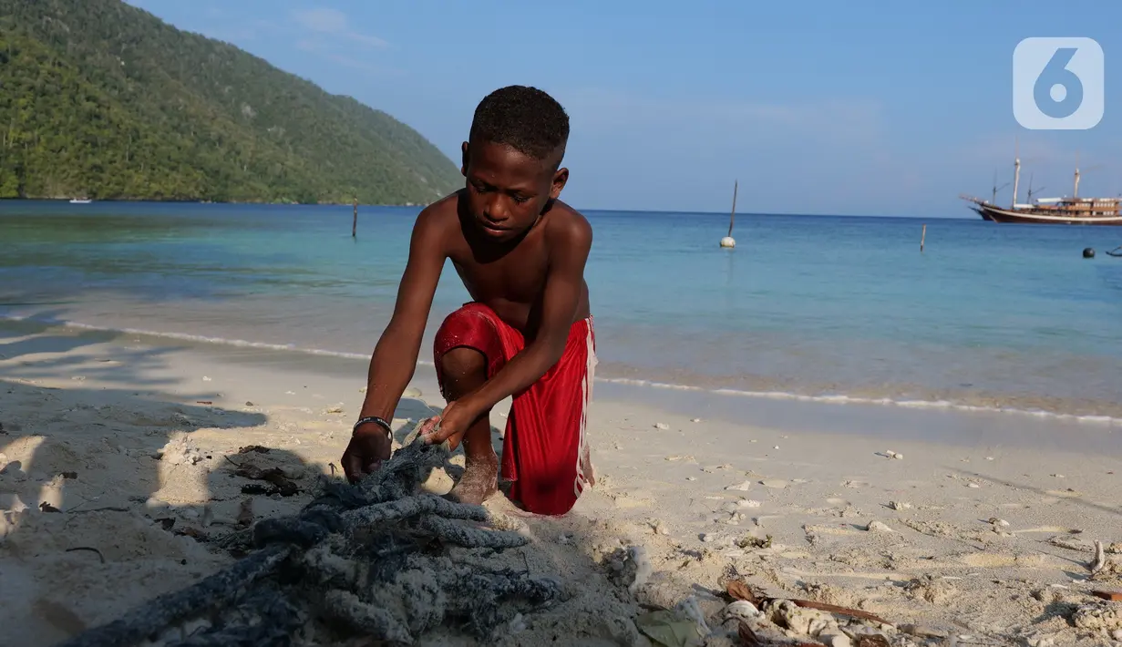 Seorang anak membersihkan sampah plastik yang ada di bibir pantai Desa Sawandarek, Raja Ampat, Papua Barat, Jumat (22/11/2019). Aksi membersihkan sampah plastik ini, digagas Carrie, aktivis asal Amerika Serikat,  yang sudah menetap di Indonesia selama 3 tahun. (Liputan6.com/Herman Zakharia)