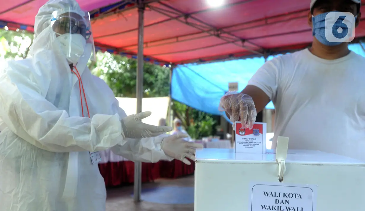 Petugas Kelompok Penyelenggara Pemungutan Suara (KPPS) dengan memakai baju hazmat membantu pemilih memasukkan kertas suara usai menggunakan hak pilihnya dalam Pilkada Tangerang Selatan 2020 di TPS 46, Paku Jaya, Serpong Utara, Rabu (9/12/2020). (merdeka.com/Arie Basuki)