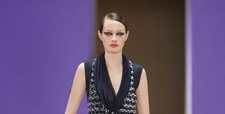 Potret busana Chanel Haute Couture Spring/Summer 2022 berikut bisa dijadikan inspirasi model baju pesta yang elegan dan mewah. Gaun warna hitam dengan detail bukaan di bagian depan ini dipadukan vest chanel berbahan tweed. Stylish dan catchy! (Dok/Chanel).