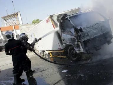 Petugas kebakaran memadamkan api yang membakar truk saat demo pemilu di Port-au-Prince, Haiti, (18/1). Warga Haiti kembali memanas setelah keputusan KPU setempat menunda pemilihan presiden ditunda hingga 24 Januari 2016. (REUTERS/Andres Martinez Casares)