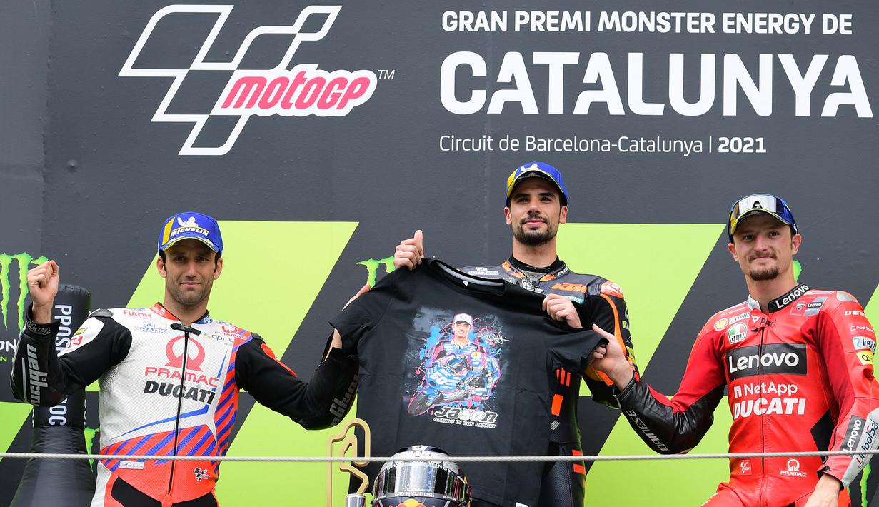 Miguel Oliviera memegang kaos bergambar pebalap Moto3 yang tewas, Jason Dupasquier bersama Johan Zarco dan Jack Miller yang finish di posisi kedua dan ketiga. (Foto: AFP/Lluis Gene)