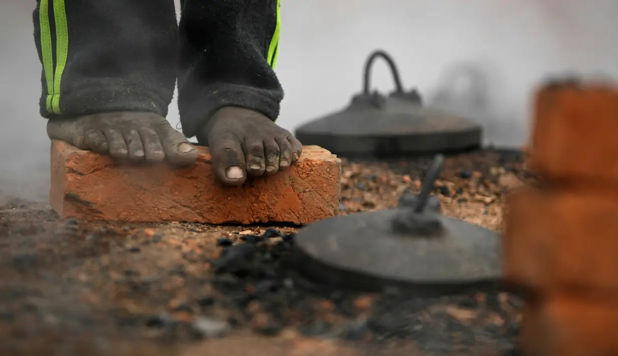 Pekerja migran India berdiri di atas batu bata dan menghangatkan dirinya di atas tungku di sebuah pabrik batu bata di pinggiran Kathmandu. Ribuan pekerja migran India datang ke Nepal untuk bekerja di pabrik batu bata. (AP Photo/Niranjan Shrestha)