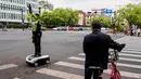 Robot-robot humanoid tersebut diterjunkan untuk membantu kepolisian mengatur arus lalu lintas dan memandu pejalan kaki, khususnya selama libur nasional Hari Buruh yang dimulai sejak 1 Mei 2026. Tampak dalam foto, seorang pesepeda melihat robot polisi humanoid di Hangzhou, provinsi Zhejiang Timur, Tiongkok pada Minggu 3 Mei 2026. (Agatha CANTRILL/AFP)