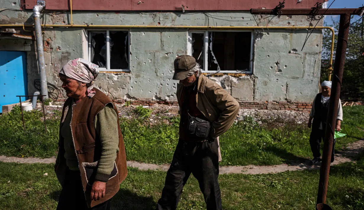 <p>Orang-orang berjalan untuk menerima bantuan kemanusiaan, di tengah invasi Rusia ke Ukraina, di desa Vilkhivka, dekat kota timur Kharkiv, pada 14 Mei 2022. Puluhan rumah di Vilkhivka, sebuah desa berpenduduk sekitar 2.000 jiwa, hancur oleh peluru, ledakan atau kebakaran. Puing-puing berserakan di jalan-jalan termasuk selongsong peluru, dan sisa-sisa amunisi. (Dimitar DILKOFF / AFP)</p>