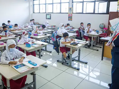 Guru memberi materi kepada siswa saat pembelajaran tatap muka (PTM) di SDN 01 Pondok Labu, Jakarta, Senin (3/1/2022). Pemprov DKI Jakarta menggelar pembelajaran tatap muka (PTM) setiap hari dengan jumlah siswa setiap kelas mencapai 100 persen dari kapasitas. (Liputan6.com/Faizal Fanani)