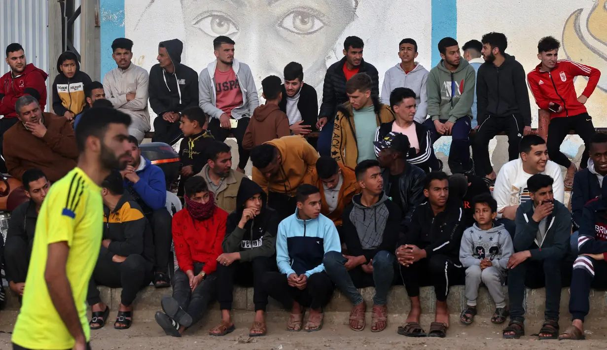 Warga Palestina menyaksikan pemuda bermain sepak bola di kamp pengungsi sebelum berbuka puasa selama bulan suci Ramadhan di Rafah, selatan Jalur Gaza (11/4/2022). Sepanjang bulan, umat Islam yang taat harus berpantang dari makanan dan minuman dari fajar hingga matahari terbenam. (AFP/Said Khatib)