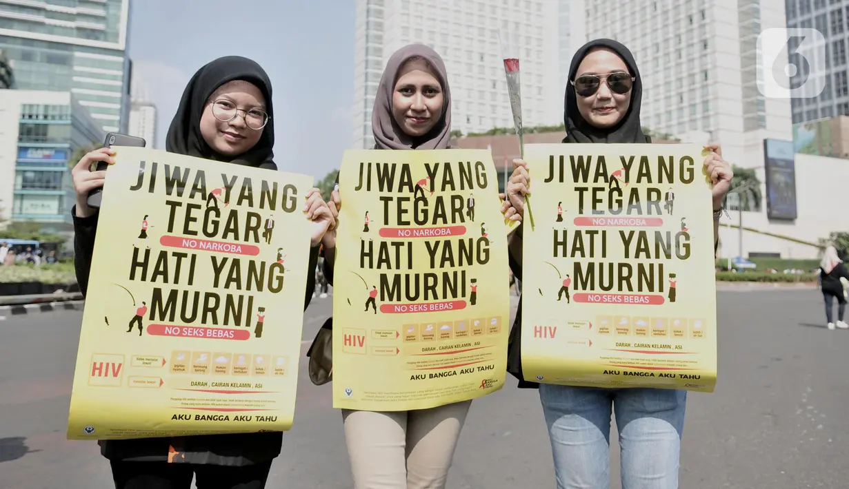 Tiga wanita menunjukkan poster saat peringatan Hari AIDS Sedunia di Bundaran HI, Jakarta, Minggu (1/12/2019). Aksi yang digelar Pemuda Pancasila dan Depkes diisi dengan bagi bunga mawar beserta buku panduan tentang penyakit AIDS kepada warga. (merdeka.com/Iqbal S. Nugroho)