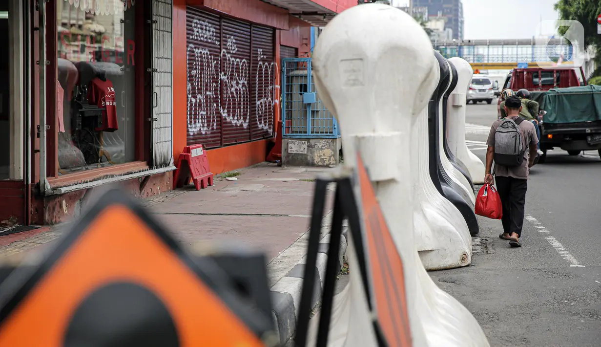 Warga berjalan kaki di samping barrier atau penghalang di kawasan Harmoni, Jakarta, Kamis (27/10/2022). Barrier yang biasa digunakan ketika terjadi demonstrasi Itu menyulitkan pejalan kaki saat melintas di trotoar. (Liputan6.com/Faizal Fanani)