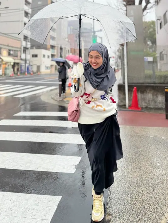 Ibu satu anak ini menyenangkan sweater putih bermotif dipadukan rok hitam panjang. Dipadukan kerudung abu-abu dan sneakers kuning. [@riaricis1795]