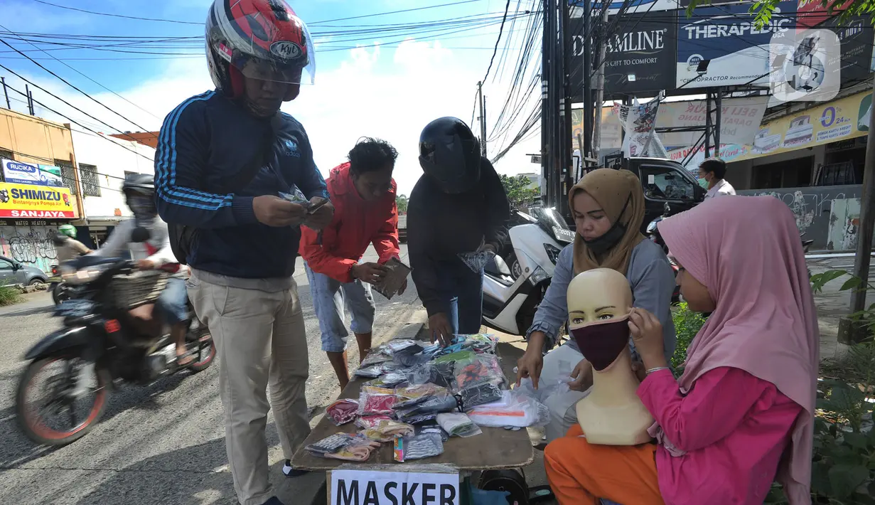Seorang ibu ditemani anaknya melayani pembeli saat berjualan masker kain buatan rumahan di Jalan Raya Cinere-Depok, Limo, Depok, Rabu (8/4/2020).  Sebelumnya ia berjualan di pasar malam, namun semenjak larangan berjualan di pasar malam ia berjualan di pinggi jalan.  (merdeka.com/Arie Basuki)