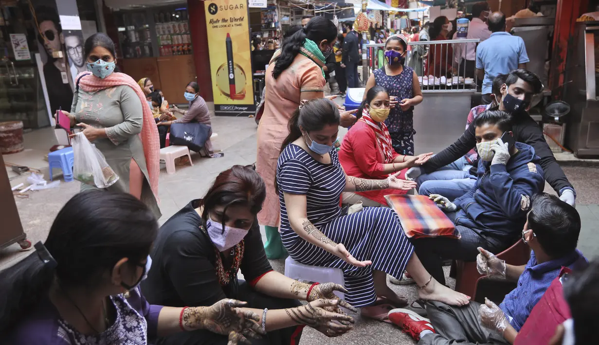 Perempuan yang mengenakan masker mendapatkan desain henna di tangan mereka pada malam festival Karva Chauth di New Delhi, India, Selasa (3/11/2020). Ini adalah festival untuk memulai bulan baru di bulan November di mana para istri akan berpuasa untuk suami-suami mereka. (AP Photo/Manish Swarup)