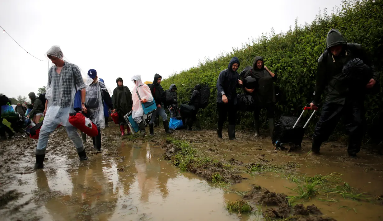 Penonton Festival Glastonbury melewati jalanan yang banjir dan berlumpur saat tiba di Worthy Farm, Somerset, Inggris, (22/6). Glastonbury Festival 2016 dimulai 22 Juni-26 Juni dengan penonton berjumlah ratusan ribu orang. (REUTERS / Stoyan  Nenov)
