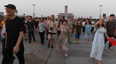 Warga berjalan menghadiri upacara pengibaran bendera saat fajar setelah kematian mantan perdana menteri China Li Peng di Lapangan Tiananmen Beijing (24/7/2019). Li Peng biasa dikenal sebagai "Jagal Beijing" meninggal di usia 90 tahun. (AFP Photo/Greg Baker)