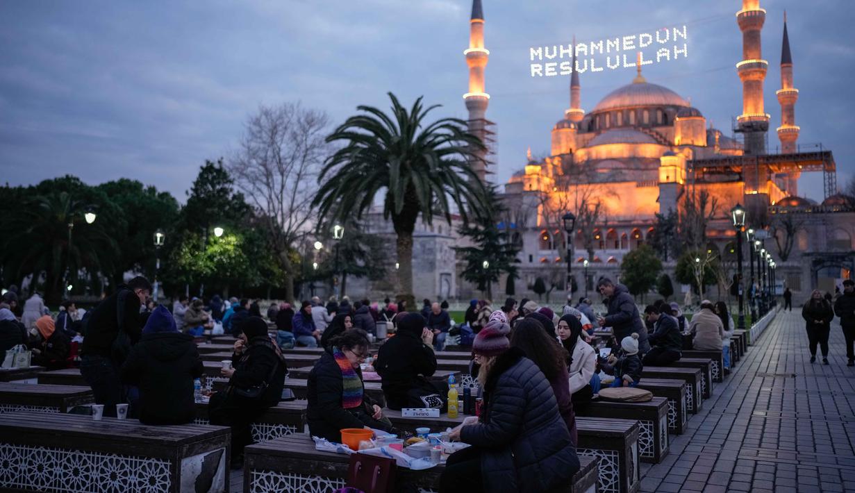 Dengan halaman yang luas dan kubah setengah lingkaran, struktur bangunan Masjid Sultanahmet menonjol baik dari segi estetika maupun teknik. Tampak dalam foto, orang-orang berbuka puasa selama bulan suci Ramadhan, di luar masjid Sultanahmet berlatar tulisan dalam bahasa Turki "Muhammad adalah utusan Allah", Istanbul, Turki, Rabu 25 Februari 2026. (AP Photo/Emrah Gurel)