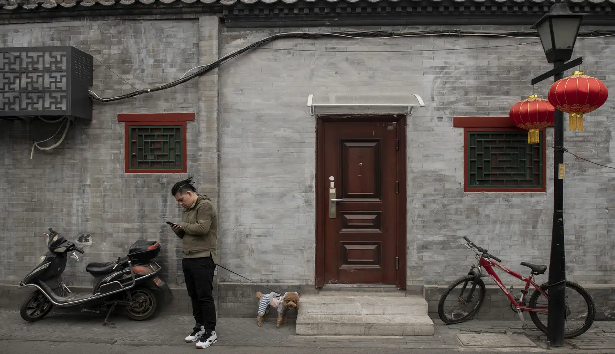 Seorang pria memeriksa ponselnya di daerah hutong di Beijing (26/2). Hutong pertama kali didirikan pada dinasti Yuan (1206–1341) dan kemudian diperluas pada dinasti Ming (1368–1628) dan Qing (1644–1908). (AFP Photo/Nicolas Asfouri)