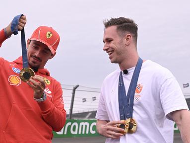 Pembalap Ferrari, Charles Leclerc berbincang sambil memegang medali emas Olimpiade Paris 2024 milik atlet balap sepeda track Belanda, Harrie Lavreysen menjelang Formula 1 GP Belanda di Sirkuit Zandvoort, Kamis (22/08/2024) waktu setempat. (AFP/John Thys)