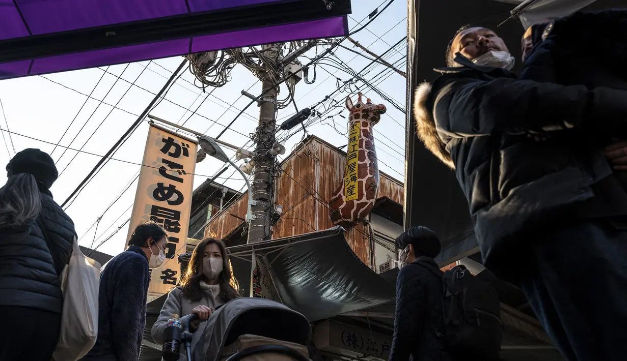 Orang-orang berjalan melalui jalan di area "pasar ikan luar" Tsukiji di Tokyo pada 28 Desember 2022. Menjelang liburan Tahun Bar, turis asing dan penduduk lokal berkunjung  ke pasar itu untuk menikmati hidangan bermacam makanan laut. (AFP/Richard A. Brooks)