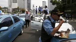 Seorang sopir taksi saat makan siang selama aksi protes terhadap aplikasi transportasi di Jakarta, Selasa (22/3). Ribuan Sopir taksi turun ke jalan. Mereka berdemonstrasi menolak keberadaan angkutan online berpelat hitam. (REUTERS/Beawiharta)