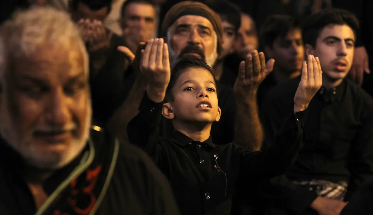 Seorang anak berdoa di lingkungan Kadhimiya yang sebagian besar penduduknya umat Syiah di ibukota Baghdad pada malam Asyura (9/9/2019). Mereka memperingati kematian Imam Hussein, cucu Nabi Muhammad yang terbunuh di Karbala. (AFP Photo/Mohammed Sawaf)