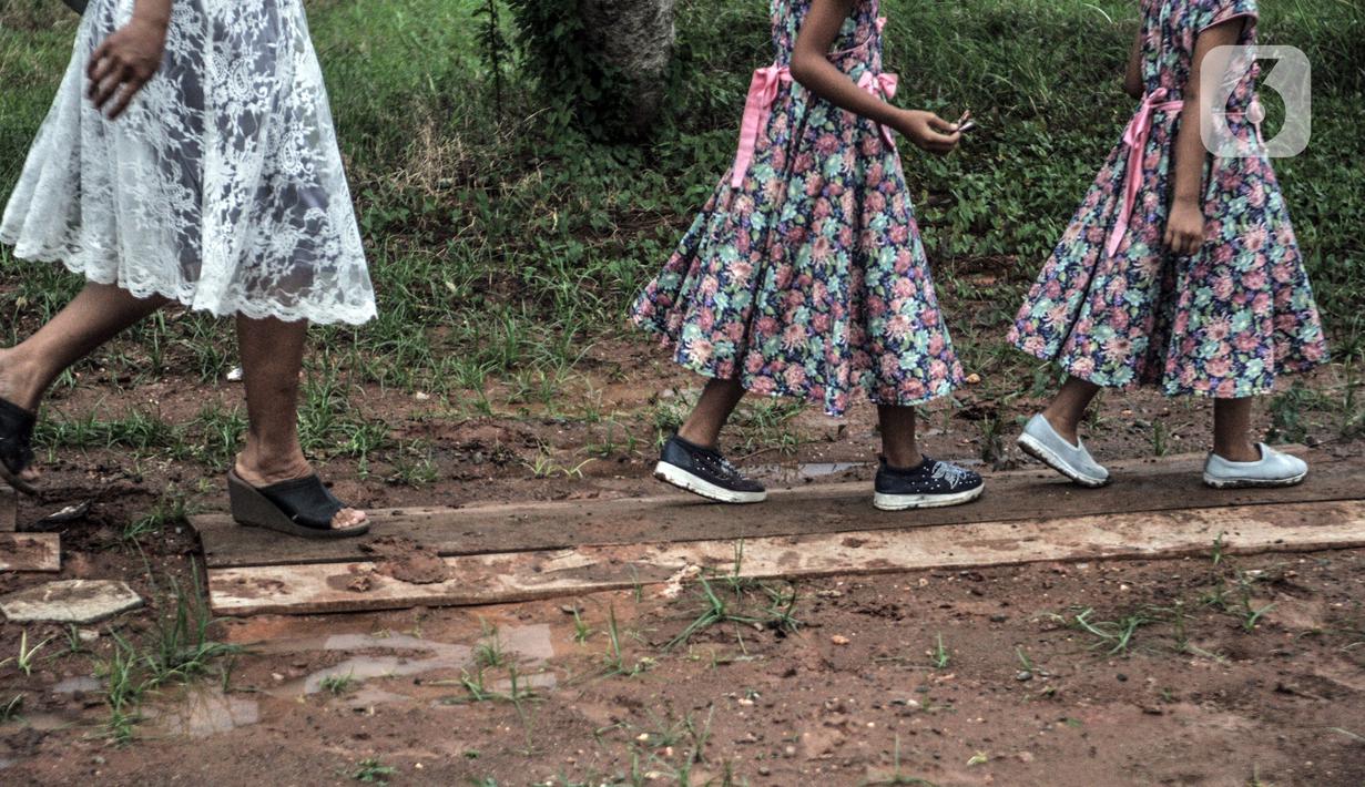 Jemaat melintasi kayu penutup jalan berlumpur saat akan mengikuti ibadah malam Natal di Gedung Serbaguna Mandiri Sejahtra CBL, Desa Sumber Jaya, Tambun, Bekasi, Jawa Barat, Kamis (24/12/2020). Banyak intimidasi yang dialami jemaat oleh sekelompok massa. (merdeka.com/Iqbal S. Nugroho)