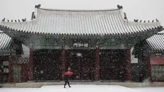 Seorang wanita menggunakan payung  berjalan saat hujan salju di Istana Gyeongbok di Seoul, Korea Selatan (13/12). Istana Gyeongbok merupakan kerajaan utama selama Dinasti Joseon dan salah satu landmark terkenal di kota tersebut. (AFP Photo/Lee Jin-man)