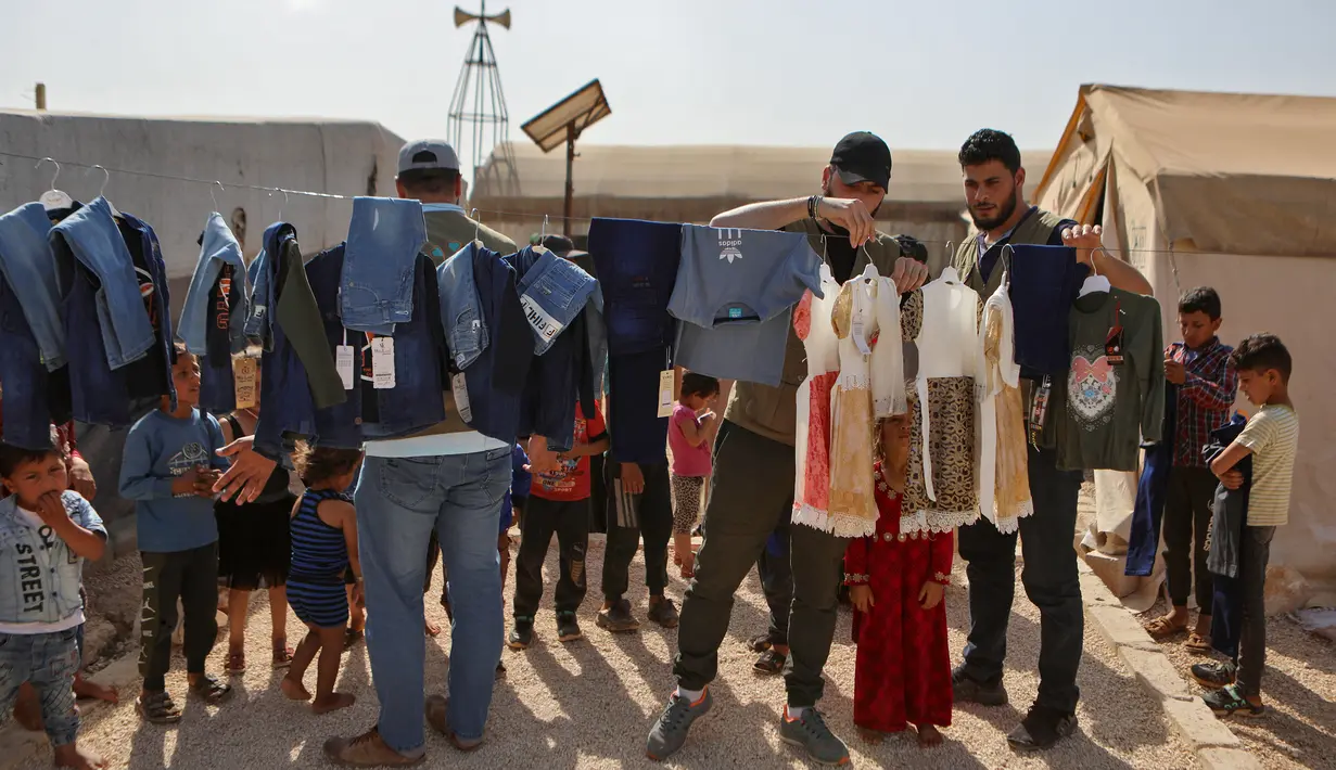 <p>Sukarelawan membagikan pakaian kepada anak-anak Suriah di sebuah kamp di pinggiran kota Dana yang dikuasai pemberontak, di sebelah timur perbatasan Turki-Suriah di provinsi barat laut Idlib (30/4/2022). Umat Islam seluruh dunia bersiap untuk merayakan Idul Fitri yang menandai akhir bulan puasa Ramadhan. (AFP/Aaref Watad)</p>
