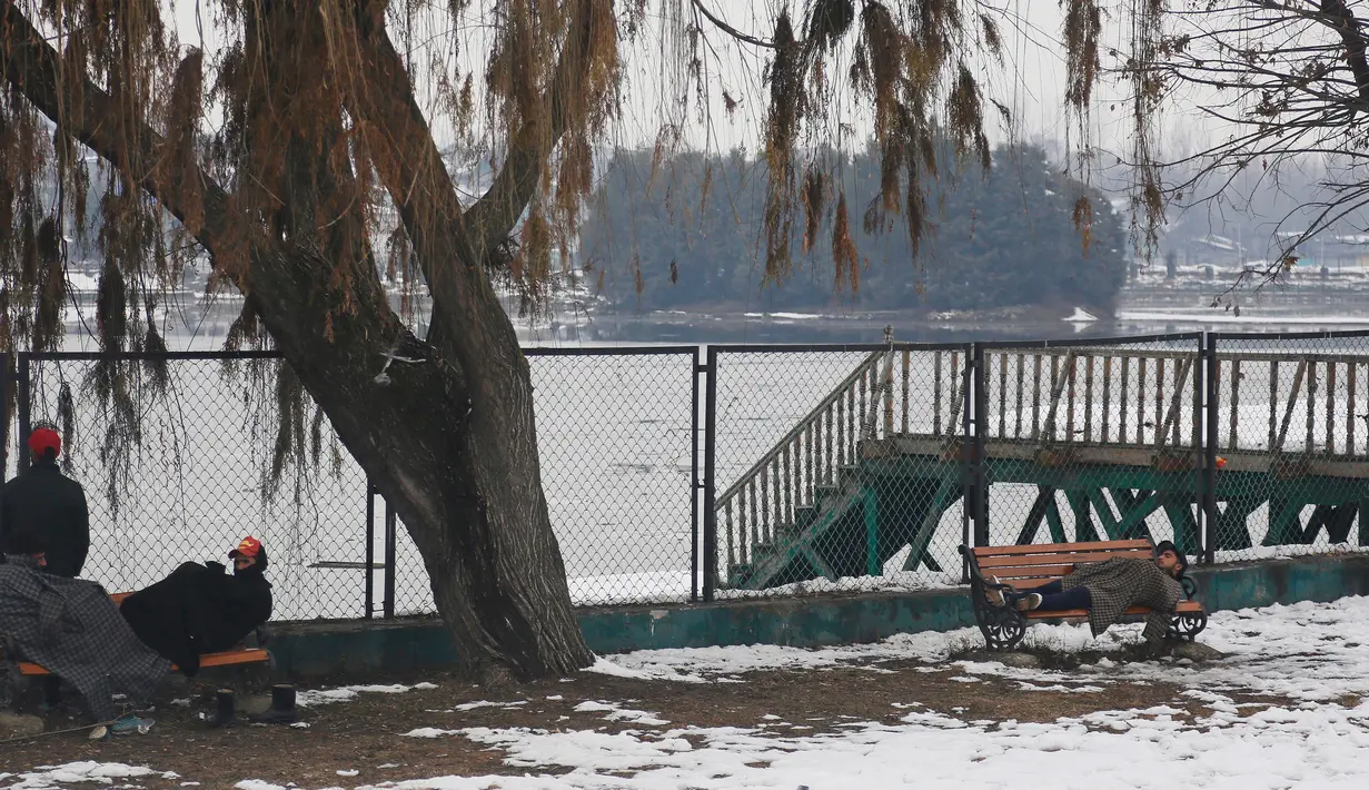 Sejumlah pria beristirahat di bangku taman yang tertutup salju di Srinagar, Kashmir yang dikuasai India (7/1). Musim salju telah mengakibatkan gangguan lalu lintas udara dan lalu lintas jalan antara Srinagar dan Jammu. (AP Photo/Mukhtar Khan)