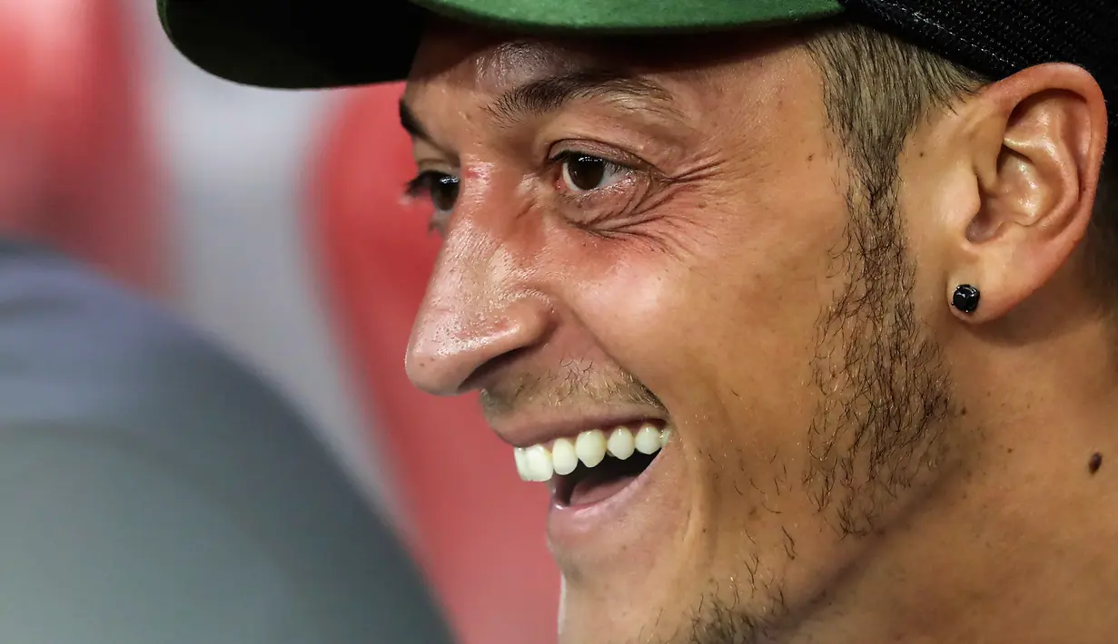 Gelandang Arsenal, Mesut Ozil tersenyum di bangku cadangan saat melihat rekannya bertanding melawan Atletico Madrid di International Champions Cup di Singapura (26/7). Arsenal kalah 3-1 setelah bermain 1-1 di waktu normal. (AP Photo/Yong Teck Lim)