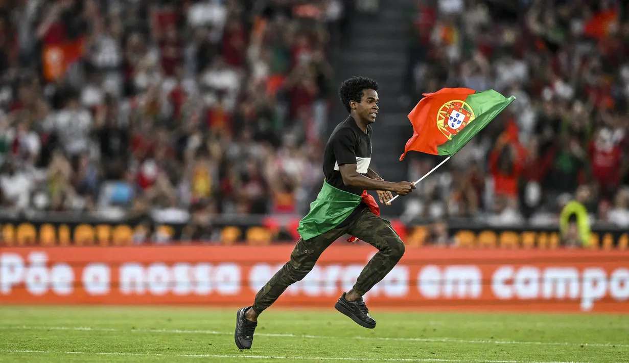 Seorang penyusup lapangan berlari sambil mengibarkan bendera Portugal di tengah laga Grup J Kualifikasi Euro 2024 antara Timnas Portugal menghadapi Bosnia Herzegovina di Luz Stadum, Lisbon, Portugal, Minggu (18/6/2023) dini hari WIB. (AFP/Patricia De Melo Moreira)