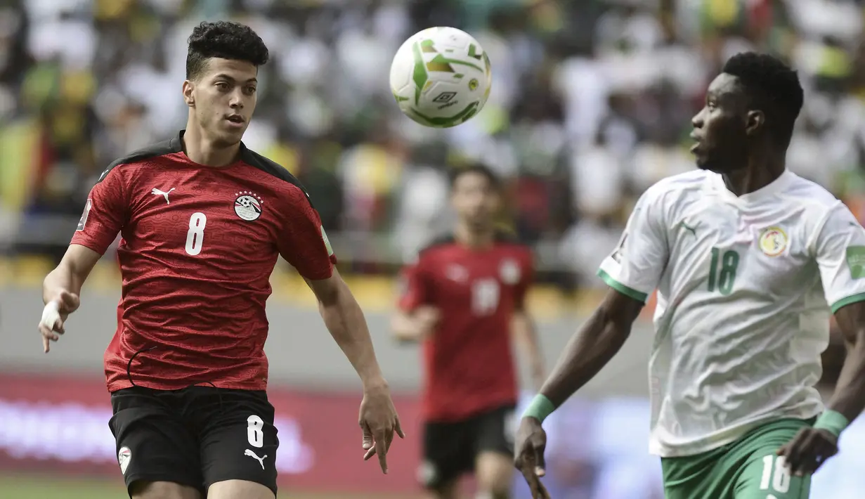 Gelandang Mesir Emam Ashour berebut bola dengan penyerang Senegal Ismaila Sarr pada Kualifikasi Piala Dunia 2022 zona Afrika di Stade Me Abdoulaye Wade, Rabu (30/3/2022) dini hari WIB. Senegal dipastikan lolos ke Piala Dunia 2022 setelah menang adu penalti atas Mesir 3-1. (SEYLLOU / AFP)