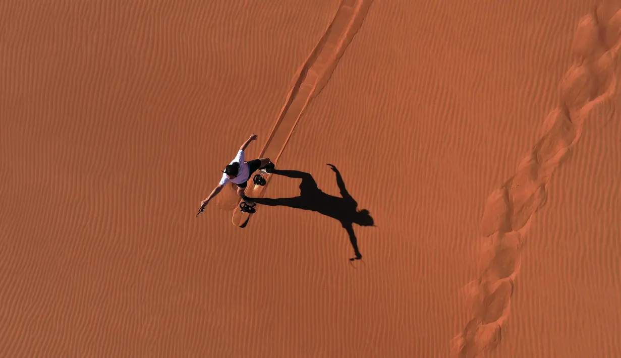 Aksi turis bermain sandboarding (papan seluncur) di gurun Dubai pada 11 Januari 2021. Di sini para wisatawan dapat mencoba sensasi bermain sandboarding sambil memandang hamparan lautan pasir cokelat. (Photo by GIUSEPPE CACACE / AFP)