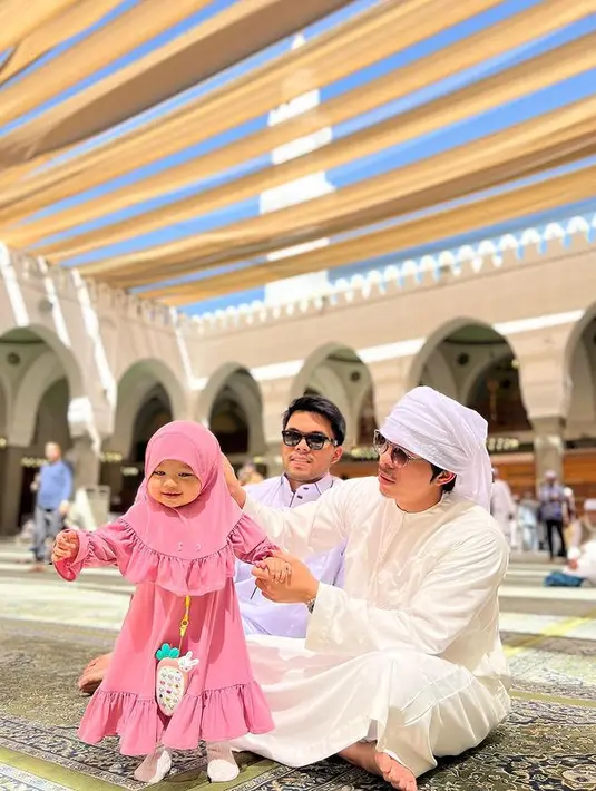 Baby Ameena yang sebelumnya sempat dikabarkan penyakitnya kambuh selama di tanah suci itu menggemaskan mengenakan dress lengkap dengan hijab warna merah muda. [Instagram/attahalilintar]