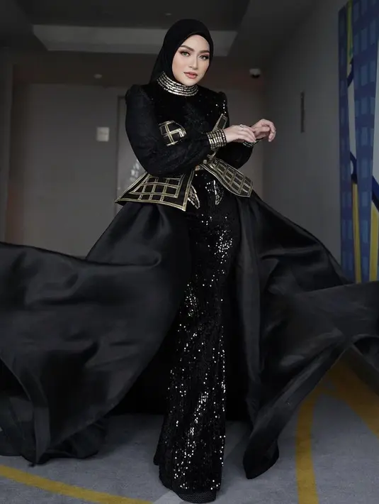 Hijab tersebut pun dipadukan dengan dress hitam sqeuin yang memiliki detail korset keemasan ditambah hiasan rok flowlynya. Nampak lehernya dihiasi kalung menumpuk emas. Credit: Instagram (@nathalieholscher)