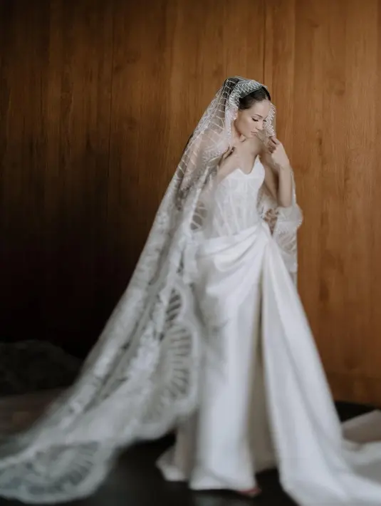 Di momen resepsi, Enzy memilih gaun klasik rancangan Monica Ivena yang hadir dengan siluet ramping dan sentuhan sulaman khas Lebanon. Dipadukan dengan veil bersulam halus sepanjang empat meter.