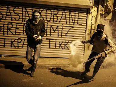 Dua militan Kurdi bersiap melemparkan tabung gas air mata ke arah polisi anti huru hara Turki dalam bentrokan di distrik Okmeydani, Istanbul (15/12/2015). Bentrokan terjadi karena pemerintah memberlakukan pembatasan jam malam. (AFP Photo/ Cagdas Erdogan)